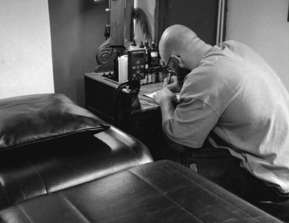 Barbe Noire Tattoo à la table à dessin, préparant un projet de tatouage sur mesure